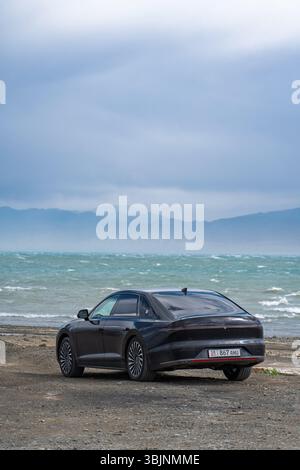 Balykchy, Kirghizistan - 12 maggio 2024: Vista posteriore di una grandezza nera Hyundai 2023 (GN7) parcheggiata su una costa rocciosa accanto a un lago ondulato con montagne Foto Stock
