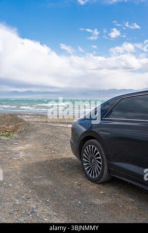 Balykchy, Kirghizistan - 12 maggio 2024: Vista posteriore di una Hyundai Grandeur nera 2023 (GN7) parcheggiata su una riva ghiaiosa accanto a un lago ondulato con mountai Foto Stock