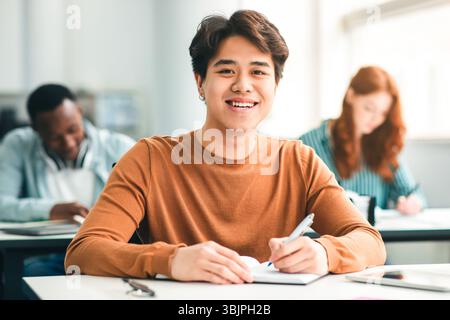 Studente asiatico di sesso maschile seduto alla scrivania in classe Foto Stock