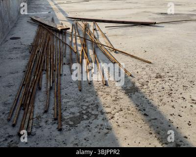 Armature arrugginite e detriti di costruzione sparsi su un terreno di cemento asciutto, riprese in prospettiva con ombre lunghe in condizioni di sole basso. Foto Stock