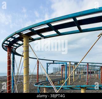 Primo piano di una struttura arrugginita di montagne russe con travi di supporto colorate vicino al mare sotto il cielo nuvoloso. Niente persone. Foto Stock