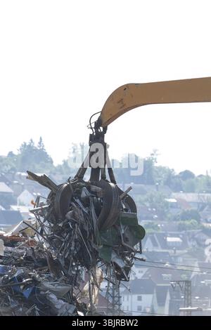 La gru idraulica solleva i rottami di metallo nel deposito di rottami sullo sfondo di una città Foto Stock