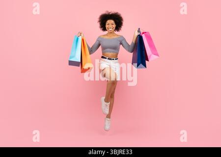 Allegra giovane donna afroamericana che salta con gioia con le colorate borse della spesa Foto Stock