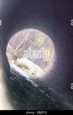 Tombini scatolari - drenare sotto la strada per un piccolo fiume. Grande tubo sotto superstrada, ingegneria autostradale, costruzione stradale. All'altra estremità del tubo, legno visibile Foto Stock