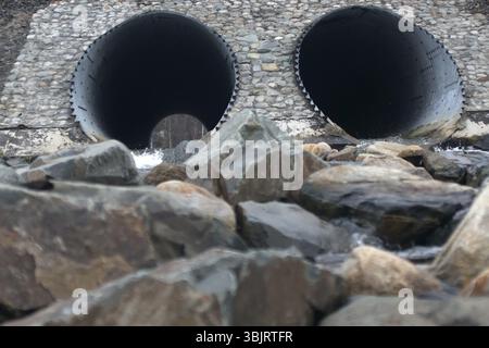 Tombini scatolari - drenare sotto la strada per un piccolo fiume. Grande tubo sotto superstrada, ingegneria autostradale, costruzione stradale. Doppio scarico. All'altra estremità del tubo, legno visibile Foto Stock