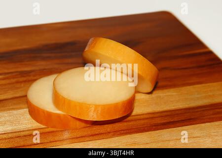 IL FORMAGGIO PROVOLONE SI AVVOLGE SU UN BORDO DI LEGNO E SFONDO BIANCO ISOLATO Foto Stock