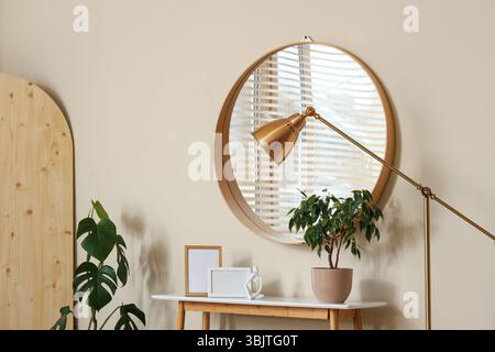 Arredi per la casa sul tavolo e riflessi di eleganti tende in legno delle finestre nello specchio appeso Foto Stock