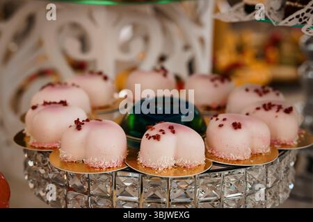 Un'immagine accattivante presenta un piedistallo in cristallo a più livelli pieno di delicati macaron rosa decorati con petali di rosa, esposto a un sontuoso ricevimento di nozze Foto Stock