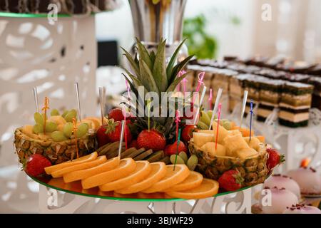 Presentazione del dessert di lusso con ananas intagliato ripieno di frutta assortita come uva, fragole, melone e fette di mango Foto Stock