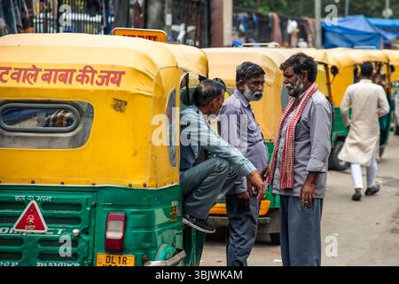 Tre autisti di risciò stanno discutendo accanto ai loro veicoli parcheggiati, rappresentando una tipica scena della vita quotidiana e dei trasporti in questo vivace ambiente Foto Stock