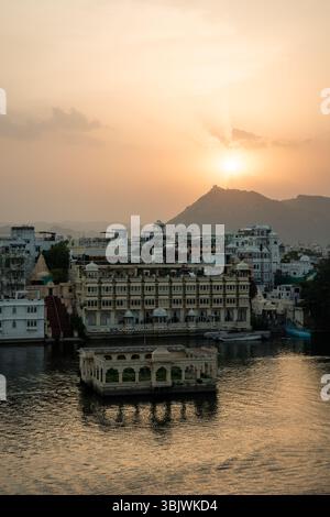 Le calde sfumature del tramonto dipingono il cielo sul lago Pichola, gettando un bagliore dorato sul Palazzo della città e sugli edifici circostanti, creando un ambiente sereno e magico Foto Stock