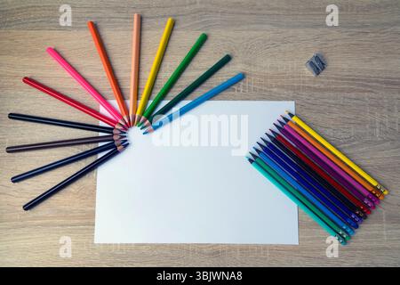 Disposizione colorata di matite su una scrivania in legno. Una varieta' di matite colorate sono disposte in un motivo artistico su una scrivania di legno. Una matita Foto Stock