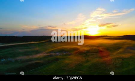 Alba su un paesaggio di campagna nebbioso con luce dorata. Una splendida vista aerea di un paesaggio di campagna all'alba, con luce dorata che scorre Foto Stock