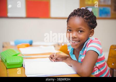 Ragazza afroamericana seduta alla scrivania della scuola scrivendo su un notebook vicino al portamatite verde, spazio fotocopie Foto Stock