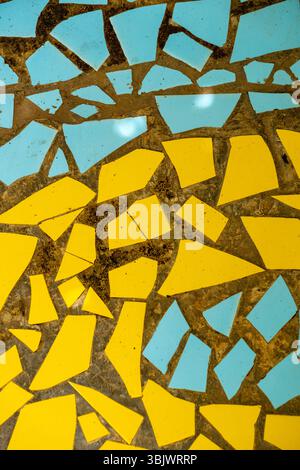 Mosaico di piastrelle gialle e blu con un quadrato blu al centro. Le piastrelle sono rotte e sparse sulla superficie Foto Stock