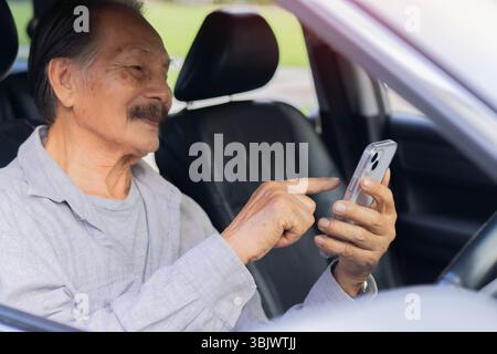 Uomo anziano felice che guida un'auto con un telefono in mano, che utilizza uno smartphone durante la guida di un'auto. Vista ravvicinata. Foto Stock