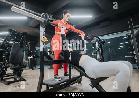 Personal trainer che assiste l'atleta nell'esercizio con pressa a panca in un moderno ambiente palestra Foto Stock