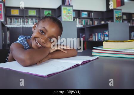 Ragazza afroamericana appoggiata sul tavolo in biblioteca studiando con quaderno e libri di testo, spazio copia Foto Stock