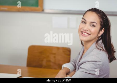 Donna che indossa un blazer grigio sorridente mentre siede alla scrivania di legno in classe con laptop e spazio per copiare Foto Stock