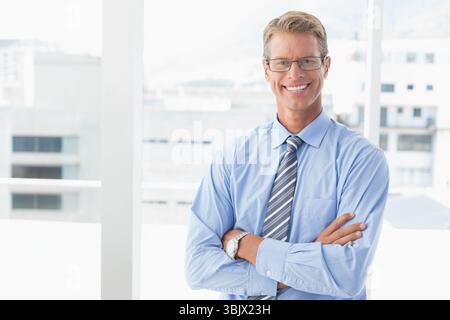 Uomo in piedi con le braccia attraversato da finestre di ufficio che mostrano lo skyline della città con cravatta e occhiali da vista a righe Foto Stock