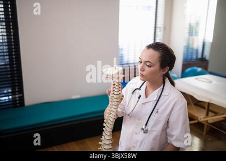 Terapeuta donna che tiene in mano il modello della colonna vertebrale e lo stetoscopio, che spiega l'anatomia nella stanza clinica, copia lo spazio Foto Stock