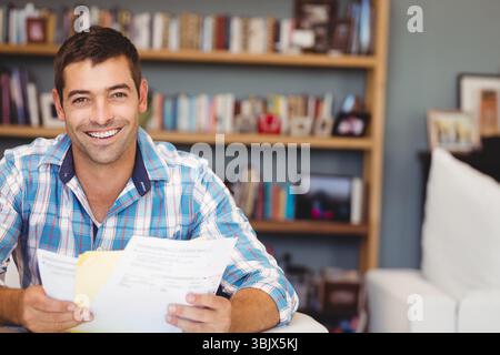 Uomo in camicia a quadri con documenti stampati, sorridente sul divano in ufficio, spazio per le copie Foto Stock