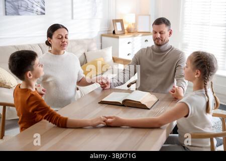 Famiglia con la Bibbia che prega a tavola all'interno Foto Stock