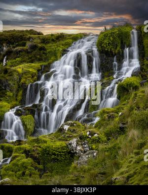 Lussureggiante paesaggio verde caratterizzato da una dolce cascata che scorre giù dalle terrazze rocciose al tramonto. Foto Stock