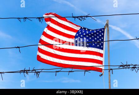 Recinzione di filo spinato di fronte alla bandiera degli Stati Uniti d'America che ondola nel vento con sfondo cielo blu Foto Stock