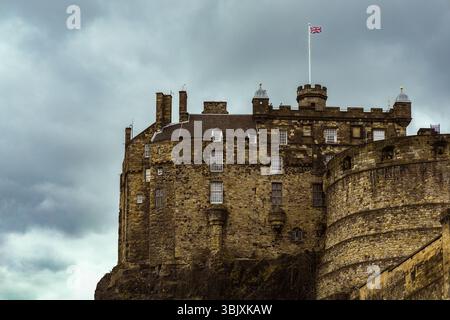 Vista dell'iconico castello di Edimburgo con la bandiera Union Jack che sventola contro le nuvole tempestose. Foto Stock