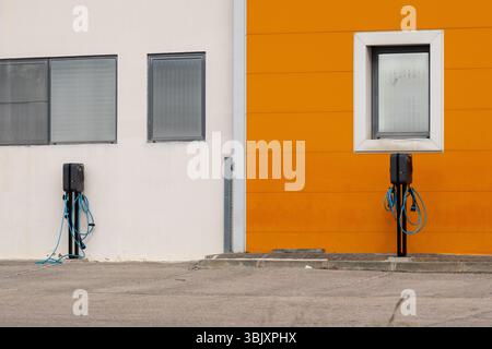 Due stazioni di ricarica per veicoli elettrici sono pronte contro un vivace edificio arancione e bianco, a simboleggiare il trasporto verde Foto Stock