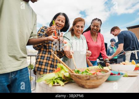 Persone multigenerazionali che fanno barbecue sul tetto di casa - amici multirazziali che si divertono a mangiare e cucinare insieme durante il giorno del fine settimana - estate e.. Foto Stock