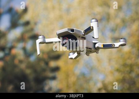 Piccolo drone volante Quadcopter in modalità volo con fotocamera all'aperto nelle giornate di sole in autunno sullo sfondo dorato del giardino Foto Stock