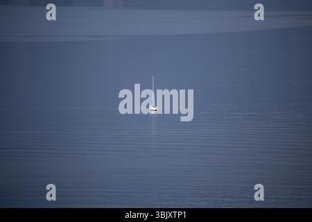 Barca a vela solitaria in acque calme e aperte sotto un cielo limpido Foto Stock