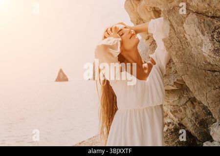 Donna, Spiaggia, tramonto - giovane donna in abito bianco gode del tramonto sulla spiaggia mentre tiene in mano una conchiglia. Foto Stock