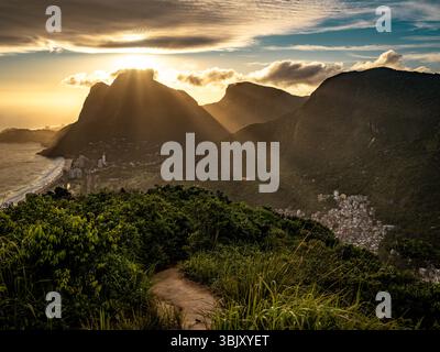 Tramonto dorato su Rio De Janeiro dalla montagna dei due Fratelli: Spettacolari raggi di sole che attraversano le vette costiere sopra l'Oceano Atlantico e Leblon Be Foto Stock