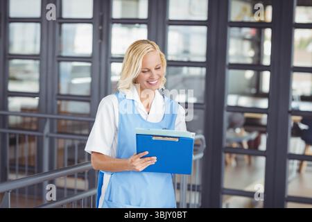 Infermiera che indossa l'uniforme blu in piedi nel corridoio della clinica tenendo gli appunti blu con i documenti Foto Stock