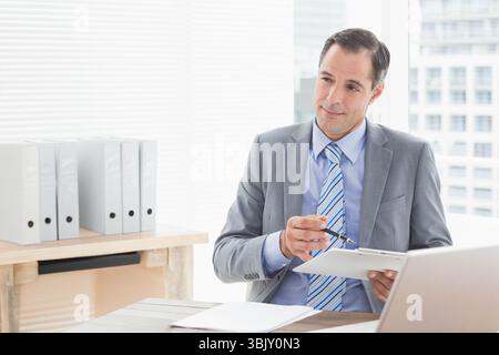 Uomo che indossa una cravatta grigia a righe con appunti che rivede i documenti alla scrivania dell'ufficio, spazio per le copie Foto Stock