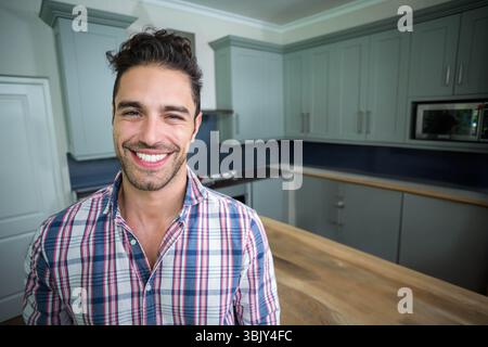 Uomo sorridente in cucina accanto all'isola di legno, armadi e scuri spruzzi, copia spazio Foto Stock