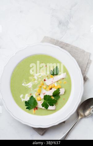 Purea di zuppa verde fatta in casa a base di broccoli, avocado, pollo e mais con panna in un piatto di ceramica rustica su backgrou di cemento bianco Foto Stock