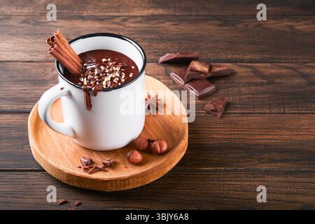 Cioccolata calda. Cioccolata calda piccante fatta in casa con cannella, nocciole tritate in tazza smaltata su un vecchio sfondo di legno. Stagione accogliente Foto Stock
