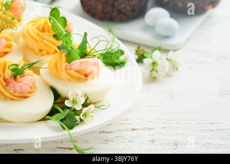 Tuorlo di uova ripiene o diavolte, gamberi, microgreen di piselli con paprika per il tavolo di pasqua decora i fiori di ciliegio o mela freschi Foto Stock