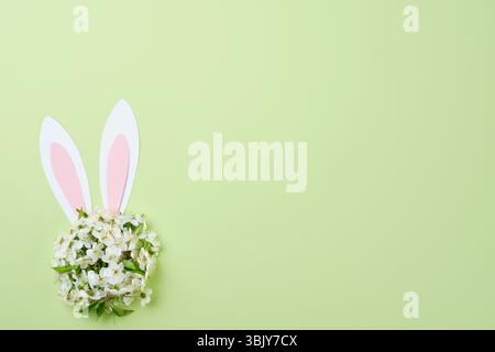 Buona Pasqua. Orecchie coniglietto di carta rosa e bouquet rotondo di fiori freschi di ciliegio o mela su backgrou verde Foto Stock