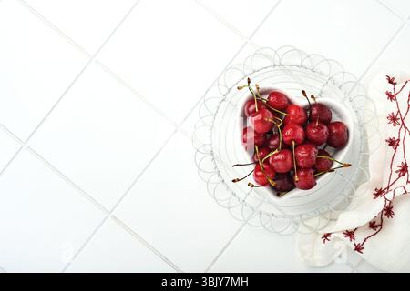 Ciliegia con gocce d'acqua su piatto a forma di cuore su tavolo in pietra bianca. Ciliegie mature fresche. Ciliegie rosse dolci. Vista dall'alto. Rustico st Foto Stock