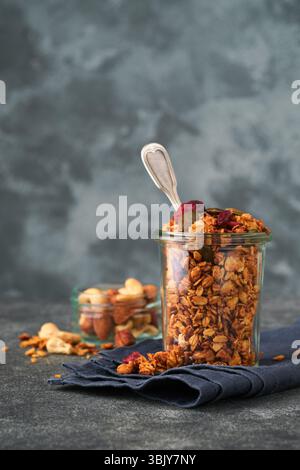 Muesli fatti in casa in vaso di vetro con yogurt greco o latte e anacardi, mandorle, zucca con semi di mirtillo essiccati in ta grigio scuro Foto Stock