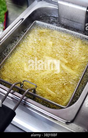 Le patatine fritte friggono in olio caldo all'interno di una friggitrice nella cucina di un ristorante Foto Stock