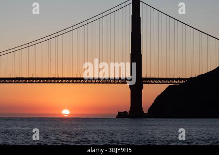 Il Golden Gate Bridge si staglia contro il sole nascente, creando un contrasto sorprendente tra la struttura artificiale e la bellezza naturale dell'alba sull'acqua. Foto Stock