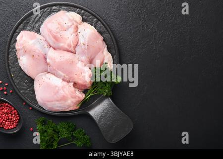Filetto di coscia di pollo crudo senza pelle con erbe e spezie su sfondo nero. Carni di pollame da allevamento. Vista superiore con spazio di copia. Mo Foto Stock