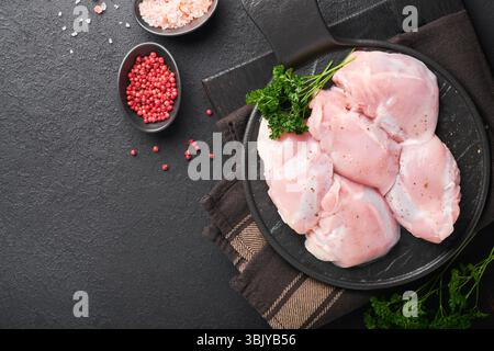 Filetto di coscia di pollo crudo senza pelle con erbe e spezie su sfondo nero. Carni di pollame da allevamento. Vista superiore con spazio di copia. Mo Foto Stock