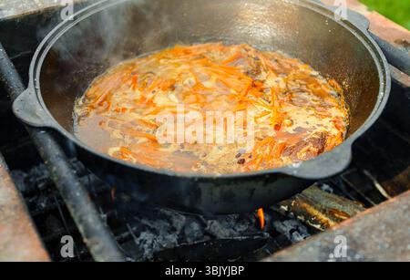 La carne con carota viene cotta nel calderone al fuoco. Cottura passo dopo passo del Pilaf. Foto Stock
